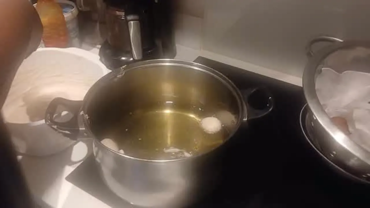 Dough balls frying in a deep pot of hot oil on a home hob.