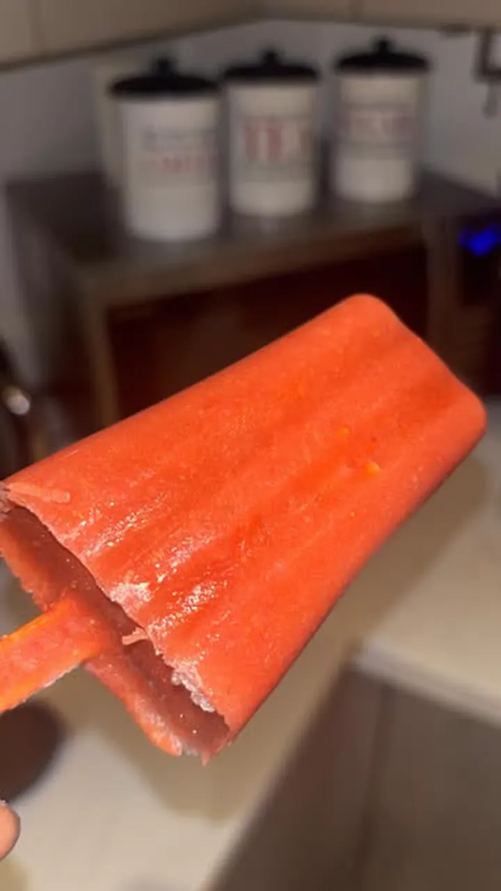 A bright orange homemade ice lolly held up in a kitchen.